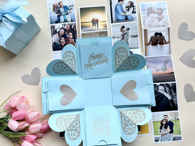 Explosion gift box for anniversary with customized pull-out album forming a photo square - Product title photo decorated with wrapped gift, flowers and paper hearts.
 
