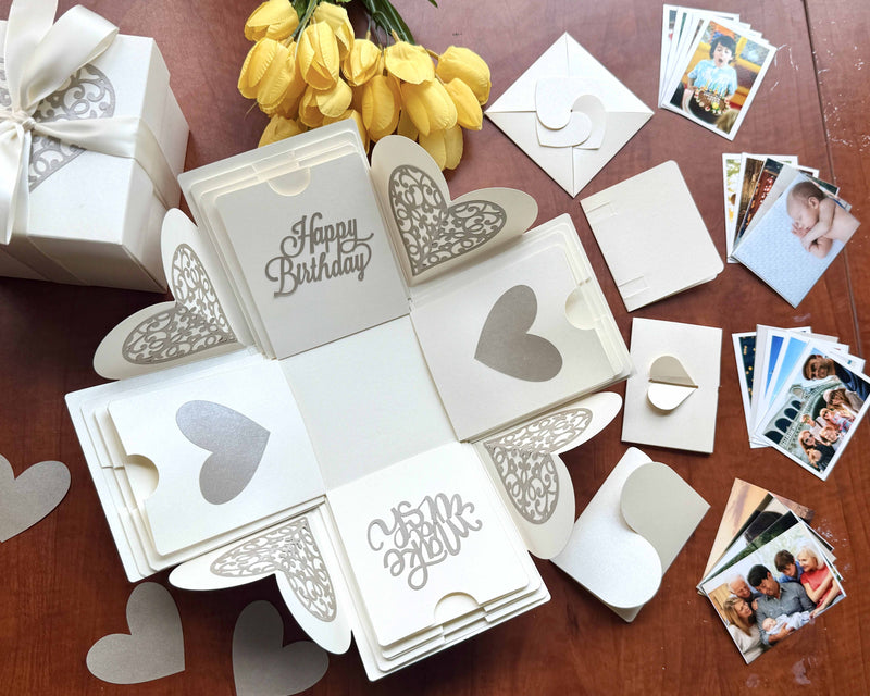 Explosion gift box for birthday white color with wallet-size photos kept inside the origami-folded pockets. Decorative product photo with wrapped gift and flower.