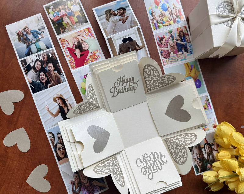 Birthday explosion gift box with customized pull-out photo albums. Decorated with wrapped gift, flowers and paper hearts. Full view.