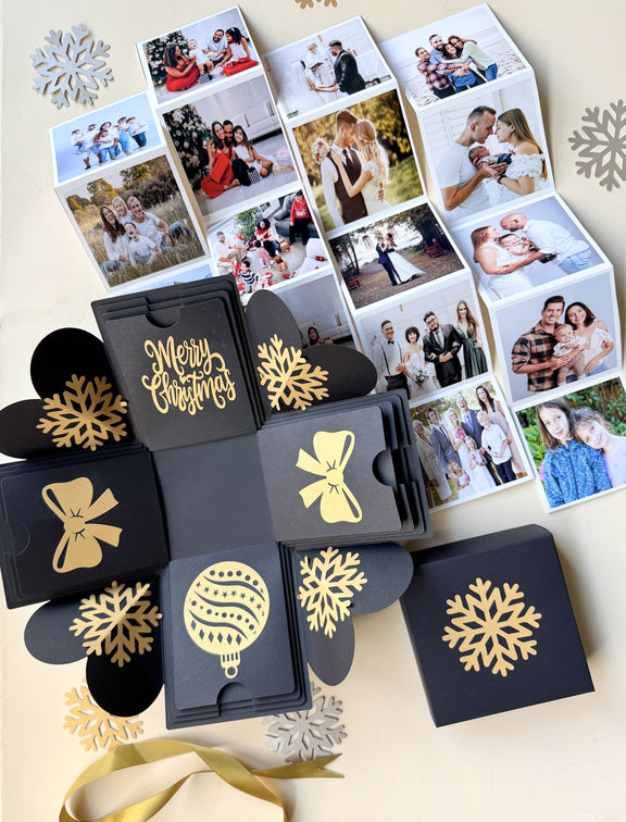 Top-view black Christmas explosion gift box showing extended pull-out photo albums.