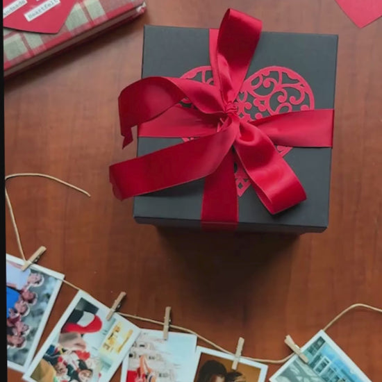 Video showing a black and red explosion gift box unfolding layer by layer, revealing photos, pull-out albums, and heartfelt message cards. The product demo highlights its customizable design and elegant craftsmanship, perfect for birthdays, anniversaries, and romantic gifting.