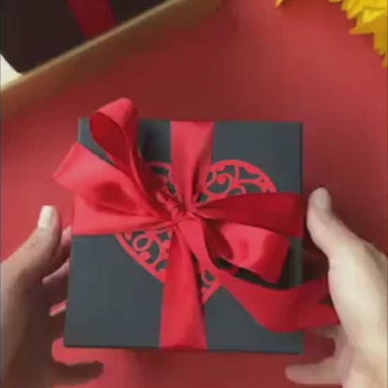 Vibrant red and black explosion gift box bursting open with photos, heartfelt messages, and pull-out albums. A luxurious handmade keepsake that captures love, joy, and celebration in every layer.
